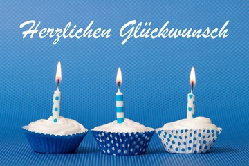 Muffins mit brennender Kerzen auf blauen Hintergrund mit Herzlichen Glückwunsch Schriftzug