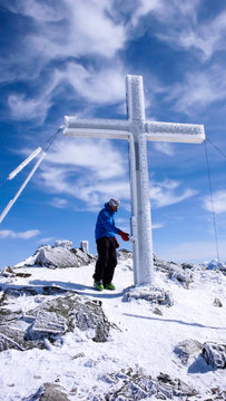 male backcountry skier on a high alpine summit preparing to write in the log book hanging on the summit cross
