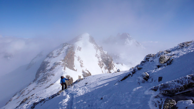 male backcountry skier hiking to a high alpine summit in Switzerland along a rock and snow ridge in light fog