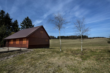 a wooden cottage and two birches on a meadow in the Moravian Highlands