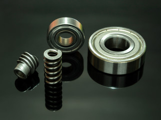 Close up view. Spare parts is spring with bearing and cog are small placed on black glass floor there is reflection.