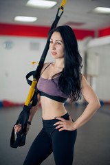Fit pretty young woman doing fly yoga stretching exercises with trx fitness straps in fitness training white gym loft classroom.