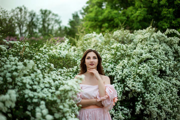 portrait of a beautiful girl in a smart dress against the background of flowering bushes close-up