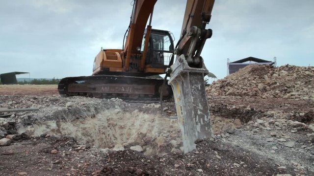 Excavator with hydraulic hammer drill at work breaking down earth for construction ground foundation