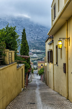 Archanes Town, Crete - Greece. Narrow paved alley with old traditional houses in Archanes on a rainy day. It is connected to Heraklion city with a 16 km long road. Storm, cloudy sky