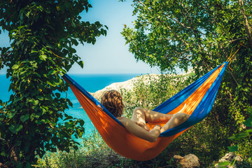 Rest. Man on vacation. The young man lies in a bright blue and orange hammock amidst the greenery...
