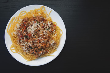 Appetizing spaghetti in a plate with Bolognese sauce on a dark background close up and copy space
