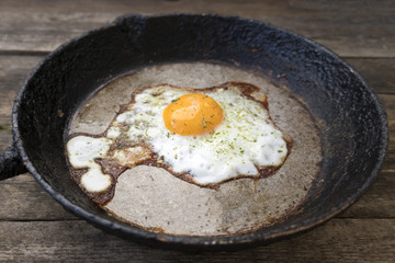 One fried egg in a frying pan on a wooden background in rustic style close-up