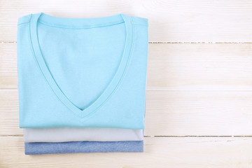 Stack of colorful perfectly folded v neck t-shirts on white wooden texture table background. Pile of different pastel color shirts and sweaters. Background, close up, top view, copy space for text.