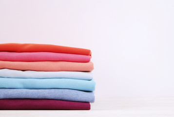 Fototapeta na wymiar Stack of colorful perfectly folded t-shirts on white wooden texture table background. Pile of different pastel color cotton shirts and sweaters. Background, close up, front view, copy space for text.