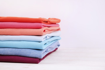 Stack of colorful perfectly folded t-shirts on white wooden texture table background. Pile of...