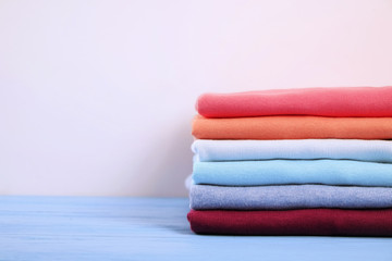 Fototapeta na wymiar Stack of colorful perfectly folded t-shirts on white wooden texture table background. Pile of different pastel color cotton shirts and sweaters. Background, close up, front view, copy space for text.