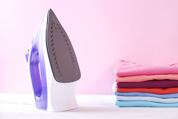 Neat stack of clean freshly laundered clothes and electric iron on pressboard. Pile of t-shirts and...