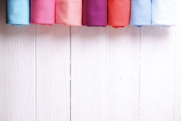 Close up of colorful clothes neatly rolled for saving luggage space, stack of cotton t-shirt rolls of different pastel colors on wooden texture table. Background, close up, copy space, top view.