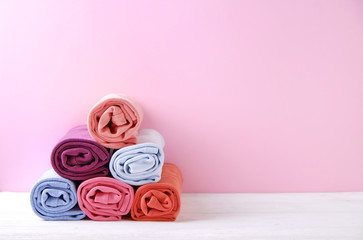 Close up of colorful clothes neatly rolled for saving luggage space, stack of cotton t-shirt rolls of different pastel colors on wooden texture table. Background, close up, copy space, top view.