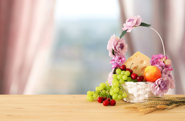 image of fruits and cheese in decorative basket with flowers over wooden table. Symbols of jewish holiday - Shavuot.