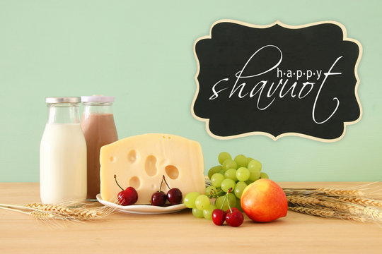 image of fruits and cheese in decorative basket with flowers over wooden table. Symbols of jewish holiday - Shavuot.