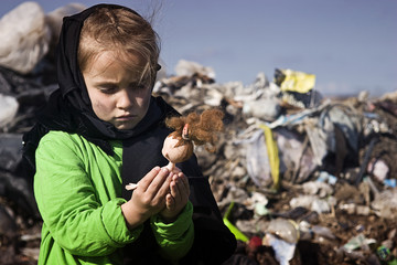 A beggar child in a garbage dump holds a broken doll in his hands