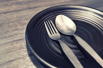 A dish black with fork and spoon silver metal in holidays dinner setting on wood background. 