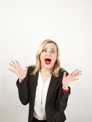 Blond female teacher wearing a strict suit keeping hands on head, terrified in panic, joking against a light background