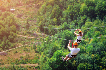 Zipline is an exciting adventure activity. Man and woman hanging on a rope-way. Tourists ride on...
