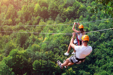 Zipline is an exciting adventure activity. Man and woman hanging on a rope-way. Tourists ride on the Zipline through the canyon of the Tara River Montenegro. Couple in helmets is riding on a cable car - Powered by Adobe