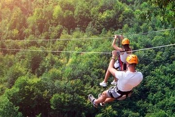 Fotobehang Zipline is an exciting adventure activity. Man and woman hanging on a rope-way. Tourists ride on the Zipline through the canyon of the Tara River Montenegro. Couple in helmets is riding on a cable car © mikeosphoto