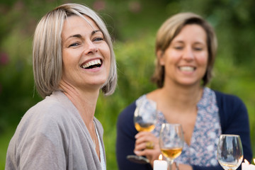 A group of friends gathered to share a meal around a table in the garden. Focus on a beautiful woman looking at the camera
