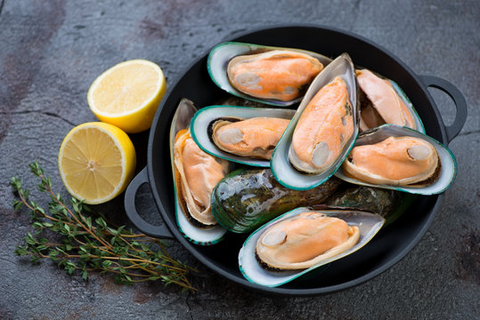 Cast-iron pan with fresh uncooked green mussels, lemon and thyme, studio shot