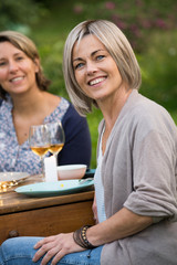 A group of friends gathered to share a meal around a table in the garden. Focus on a beautiful woman looking at the camera
