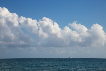 Naklejka na ściany i meble Boat Passing Left to Right on the Atlantic Ocean in Florida Beneath a Bank of Fluffy Cumulus Clouds in the Afternoon