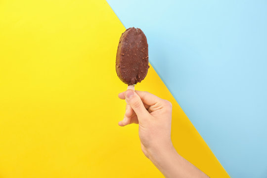 Man holding yummy ice cream on color background. Focus on hand