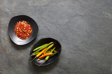Ground dried chilli peppers with fresh peppers in black bowls with copy space