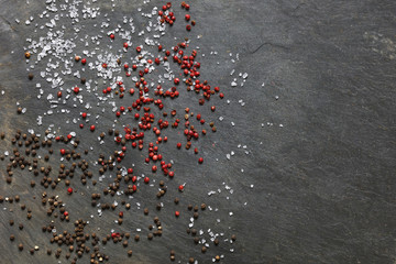 Rock sea salt  scattered with brown and pink peppercorns on slate background with copy space to right
