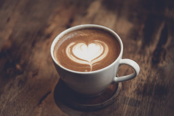 White cup of coffee with heart shape and aromatic smell on the table brown wood.