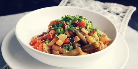 Vegetable stew with potato, carrot and green beans topped with sesame seeds. European cuisine. Healthy vegan lunch on the round white plate. European cuisine. Vegetarian. Wide photo.