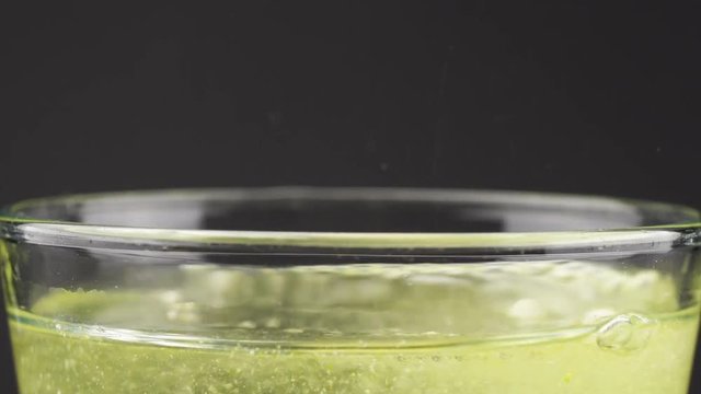 An yellow effervescent tablet against pain falls into a glass and dissolves slow-motion shot of aspirin on a colored background