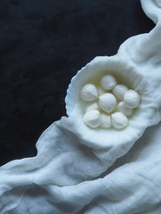 Fresh homemade mozzarella cheese in cheesecloth on the black texture background. Top view, space