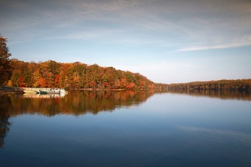 Naklejka na ściany i meble Barge on the Water Overlooking Trees with Leaves Changing Color from Green to Red in Burke Lake Park, Virginia