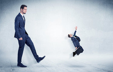 Big businessman kicking small businessman who is flying away with his briefcase on his hand
