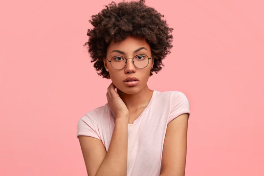 Studio shot of good looking African American female freelancer works distantly at home, dressed casually, has crisp hair, looks seriously and thoughtfully at camera, tries to concentrate on new task