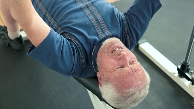 Mature man doing chest press exercise. Aged man doing efforts to lift weight in gym. Hard training for muscles.