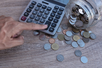 Coins spilling out of a glass bottle and calculator on wood table in morning time with financial...