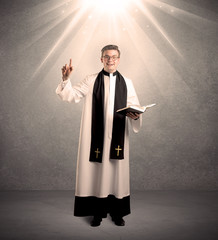 A male religious young priest in black and white dress giving his blessing, holding the holy bible...