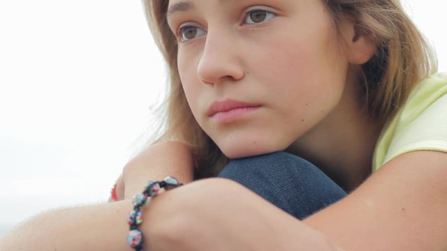 Close up portrait of sad depressed teenage girl sitting down alone outdoors