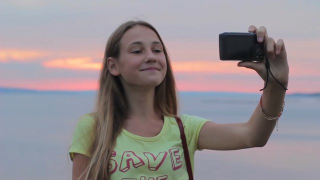 Teenage girl taking self portrait with hand-held digital camera outdoors