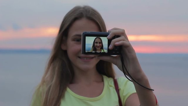 Teenage girl making selfie portrait with camera at sunset