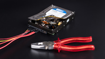 Hard disk drive and pliers on black background. Open storage device with secret informations. Idea...