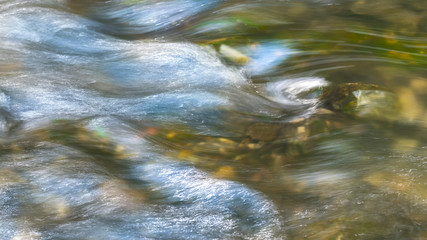 Background from flowing water surface. Artistic close-up of running swift creek. Abstract playful...