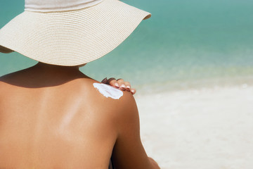 Woman applying sunscreen creme on  tanned  shoulder. Skincare. Body Sun protection suncream. Bikini hat woman applying moisturizing sunscreen lotion on back.